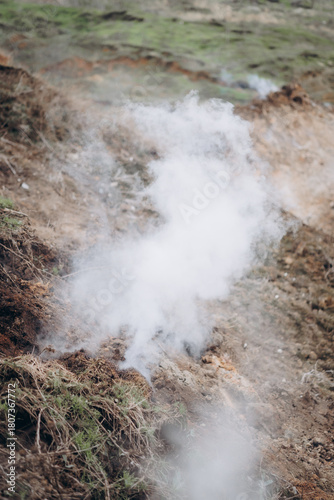 A rugged hillside emits white smoke from multiple cracks in the earth, creating a dramatic and surreal atmosphere.