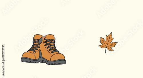 Pair of brown hiking boots placed next to a single fallen autumn maple leaf on a beige background.