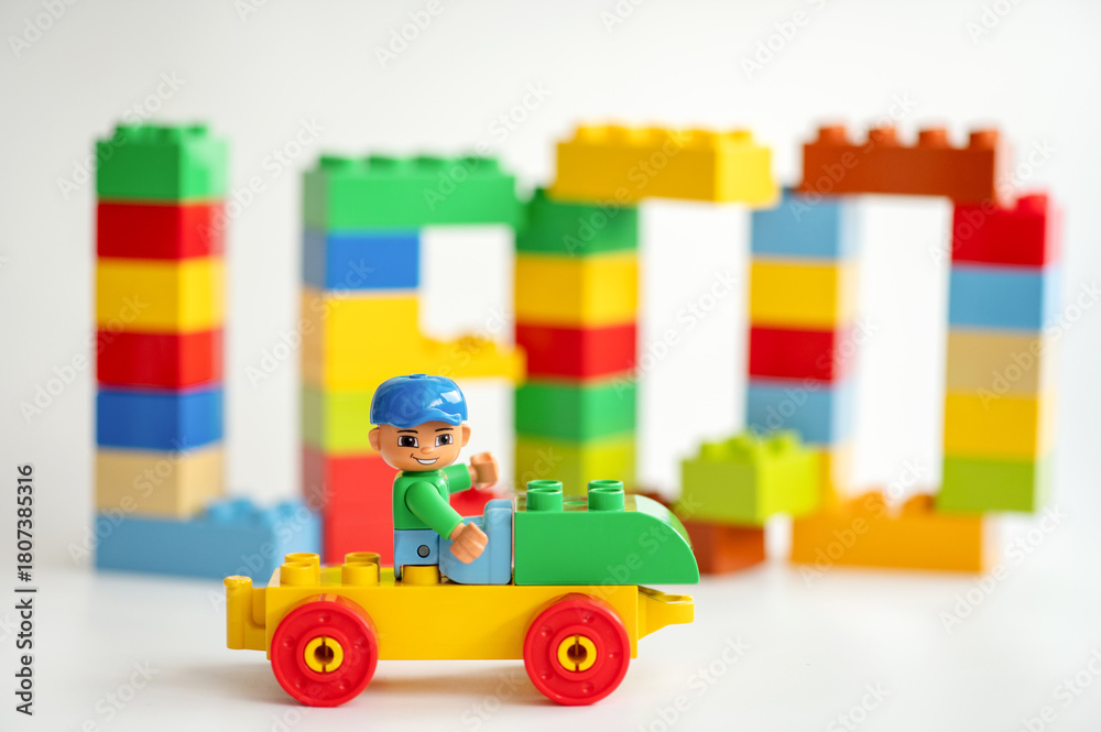 Naklejka premium A Lego construction worker minifigure sits on a toy car in front of Lego bricks on a white background