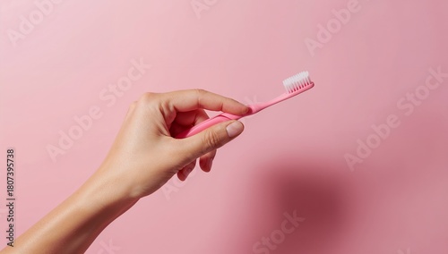 Hand holding a pink toothbrush on pastel pink background