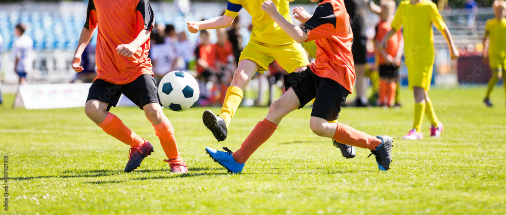 Fototapeta premium Kids Playing Competitive Soccer. Youth Players in Soccer Jerseys Running Toward Soccer Ball and Kicking Ball Towards Goal. Kids Have Fun During Football Match