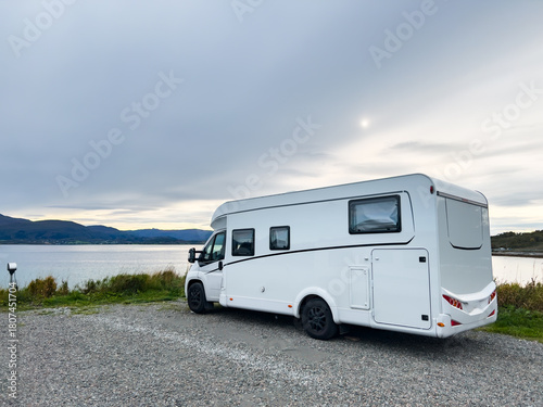 White camper van parked near a tranquil lake and mountains, offering a serene escape for travel and leisure