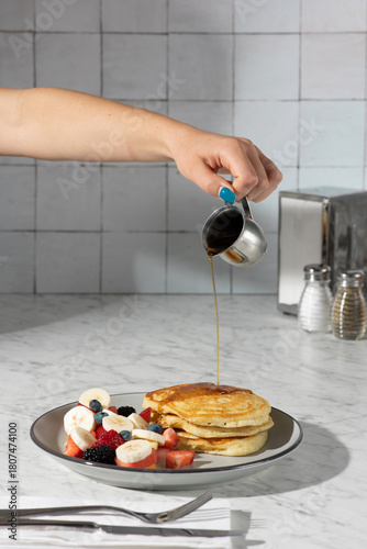 hand pouring syrup on pancakes in hard light