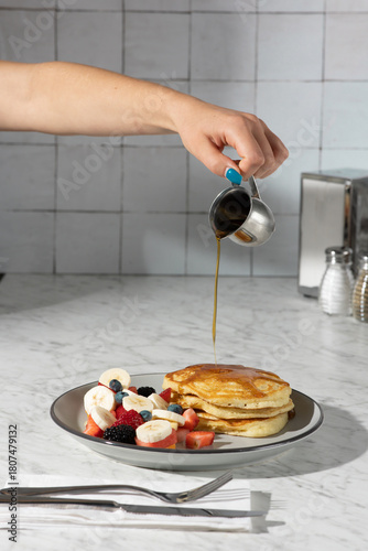 hand pouring syrup on pancakes in hard light