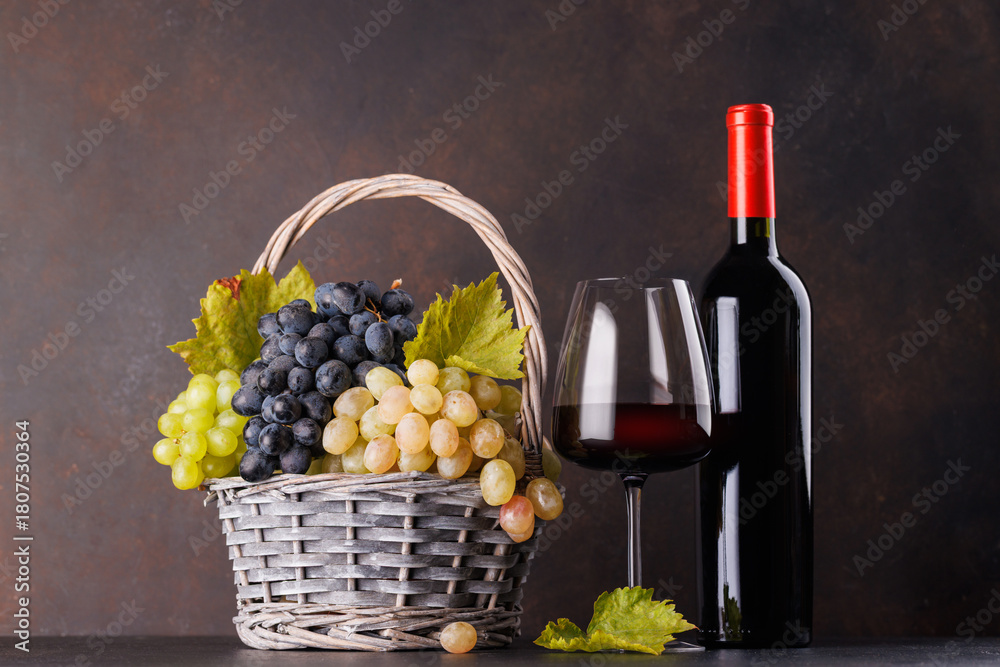 Naklejka premium Red wine bottle with a glass and basket of fresh grapes