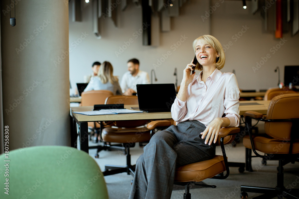 Obraz premium Young professional smiling while talking on phone in modern office environment