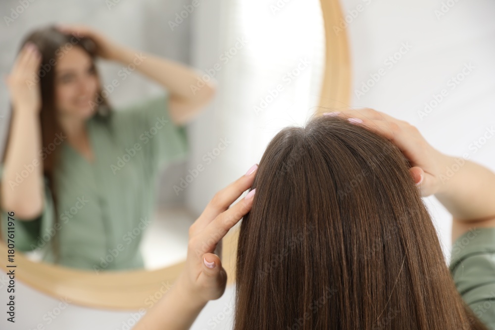 Fototapeta premium Woman using talcum powder as dry shampoo near mirror at home
