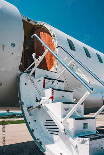 Close-up view of an aircraft airstair and open cabin door, photographed from a low front angle in bright daylight. The focus is on steps, handrails, and door structure.