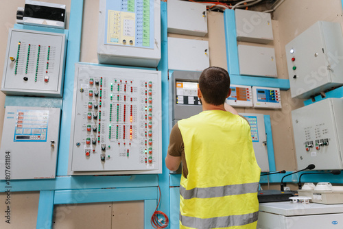 Technician checking control panels with indicator lights in industrial control room