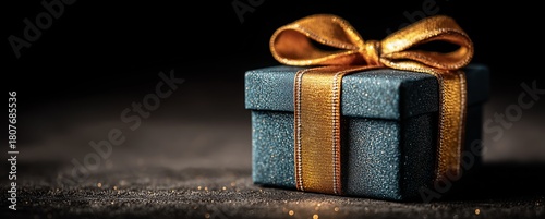 Beautifully Wrapped Gift Box With Golden Ribbon on Dark Background During Hol...