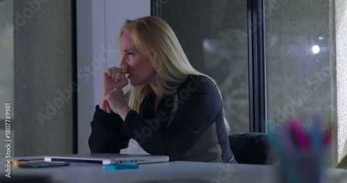 Business woman seated with hand to forehead, overwhelmed by work pressure and fatigue during intense moment of stress in quiet modern office