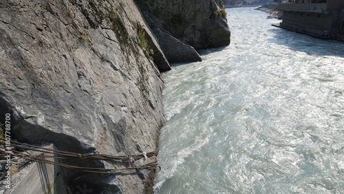 Dramatic photograph of a steep rocky cliff face above a turbulent white river, obstacle concept.