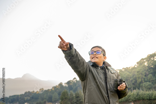 Young boy in glasses pointing and holding binoculars, exploring nature, adventure concepts