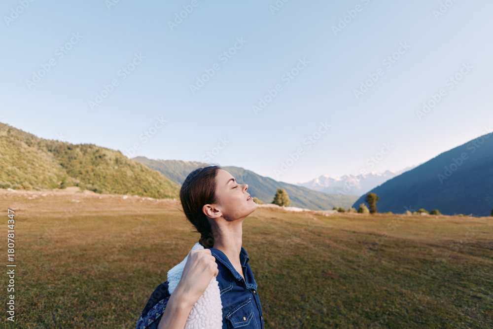 Fototapeta premium Woman with backpack in mountain meadow enjoying fresh air and nature, hiking and travel portrait with closed eyes, peaceful scenic landscape and relaxed outdoor adventure.