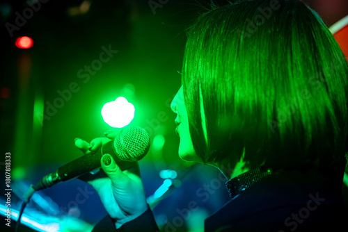 Konstfotografi Female singer performing on stage with vibrant green lighting