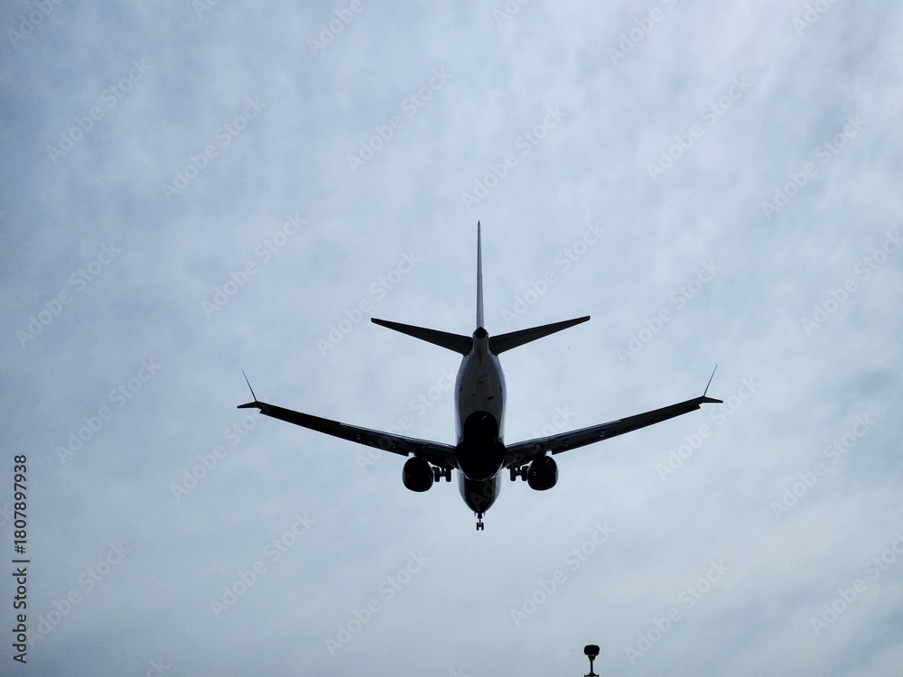 Fototapeta premium Airplane landing silhouette against cloudy sky. A commercial passenger jet captured from below while approaching the runway.