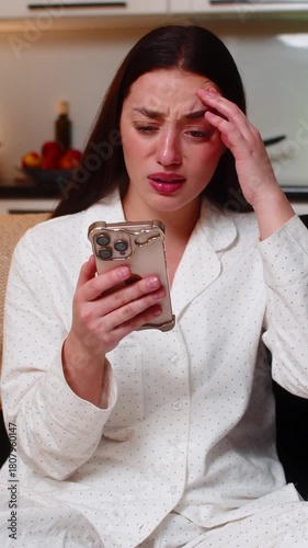 Young woman scrolls smartphone at night home sees lose alert from online game or lottery feels upset. Caucasian girl on sofa at evening frowns shakes head sighs shows disappointment mood after loss.