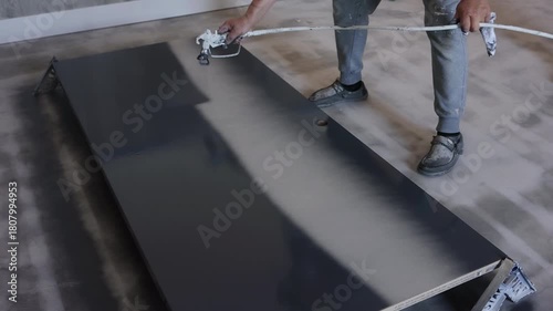 Worker uses spray gun to apply paint on wooden door surface in during paint day.