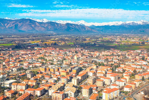 Fototapeta Naklejka Na Ścianę i Meble -  Torino area of Venaria Reale with red-tiled buildings spread across the plain, framed by distant snow-capped Alps. Urban density contrasts beautifully with the wide natural mountain backdrop