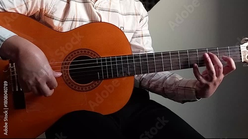 A man playing tremolo fingerstyle technique with classic guitar and changing notes on the fretboard  with his left hand from a forward angle near sunset