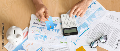 Young man in debt with credit card using calculator at table, top view