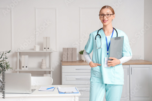Happy female doctor with laptop, stethoscope and clipboard in clinic