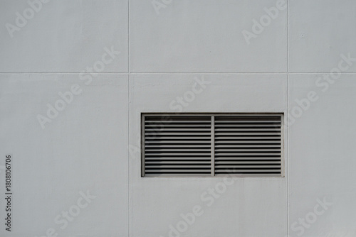 Rectangular metal ventilation grille on gray textured wall, minimalist industrial exterior detail.