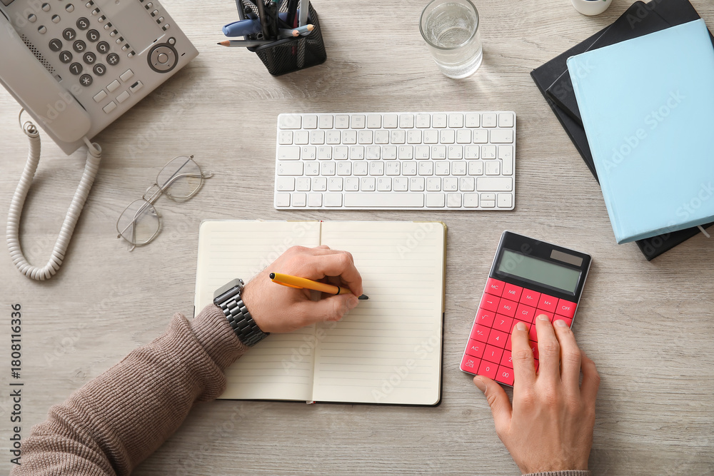 Obraz premium Male hands using calculator and doing notes in office. Top view