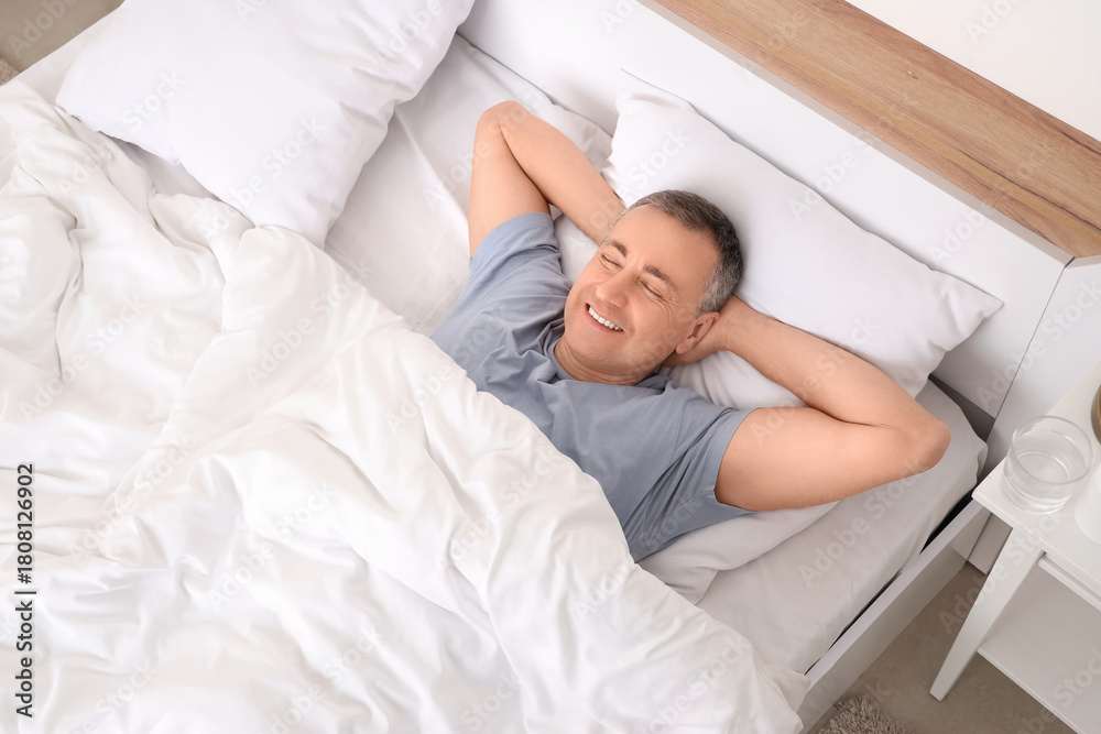 Naklejka premium Mature man lying under blanket in bedroom, top view