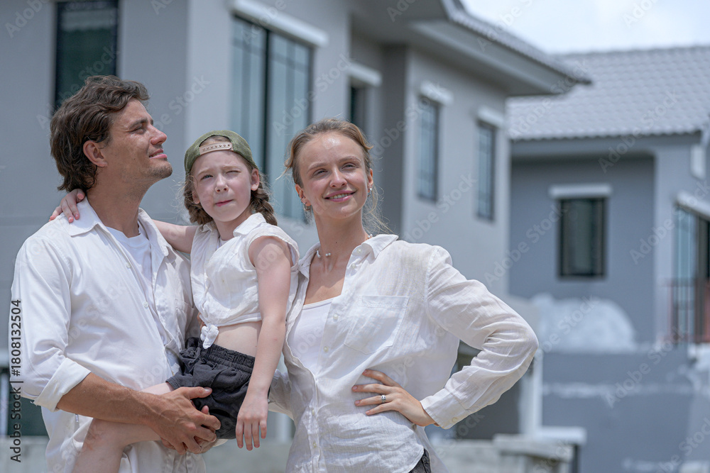 Obraz premium A hopeful young family looks towards their future outside a new modern home. The father holds their daughter, who points excitedly, as the mother smiles, dreaming of their life together.