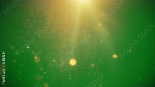 A radiant golden sunbeam illuminates sparkling dust particles and soft bokeh against a vibrant green background.
