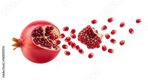 A whole ripe pomegranate with a broken piece scattering an explosion of fresh ruby-red seeds, isolated on a white background
