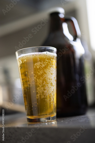 Bubbly glass of beer next to glass growler container, beer in a sunny kitchen, home brew