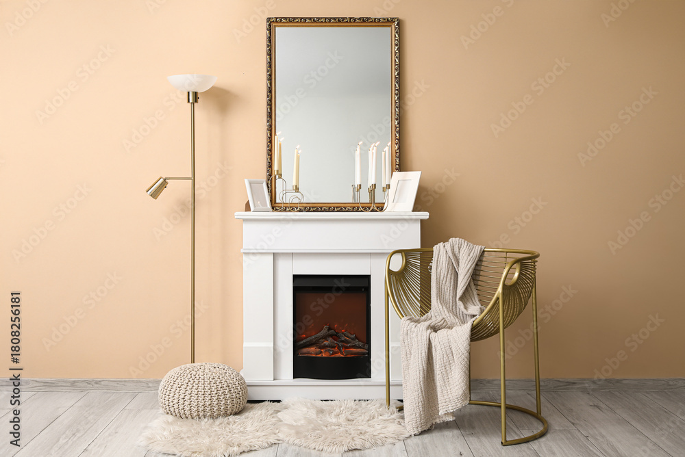 Fototapeta premium Interior of living room with armchair, lamp, mirror and candle holders on fireplace near beige wall