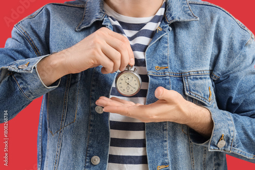 Young man with stopwatch on red background, closeup