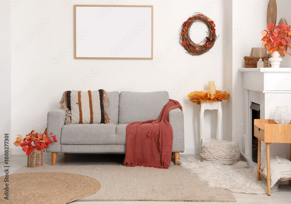 Fototapeta premium Comfortable sofa, fireplace and decor with autumn leaves in interior of living room