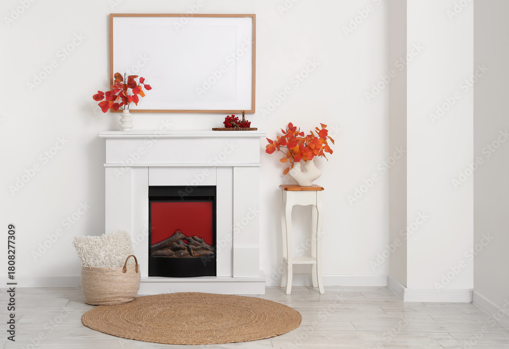 Fototapeta premium Fireplace, photo frame and vases with autumn leaves in interior of living room
