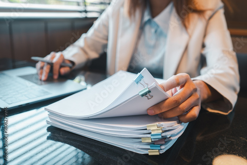 Bilde på lerret A business professional in a white blazer reviews documents at a desk with a laptop, highlighting a modern office environment