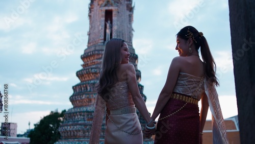Photography Thai women holding hands, smiling at wat arun temple, wearing chut thai