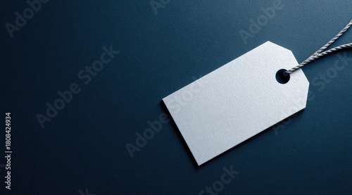 Blank white tag with string on dark, moody blue surface