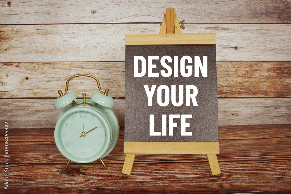 Naklejka premium Design Your Life text on easel blackboard with alarm clock on wooden background