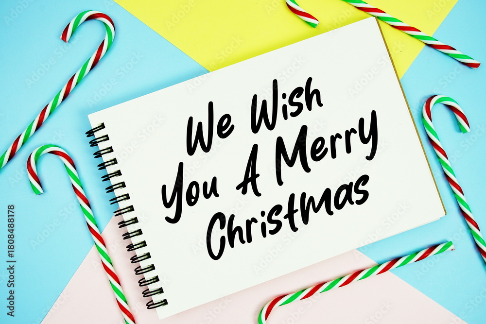 Obraz premium We Wish You A Merry Christmas message of season holidays written on notepad with candy cane decoration on pastel background