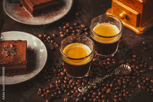 Two espresso coffee mugs with piece of chocolate cake on brown background