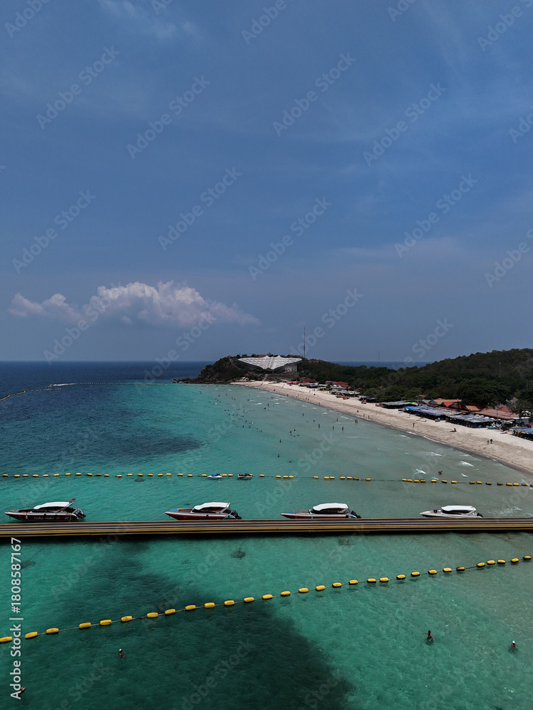 Obraz premium Aerial drone view of Samae Beach (Hat Samae) on Koh Larn (Coral Island), Pattaya, Thailand. The image captures long floating pontoon pier extending into the sea, lined with speedboats.
