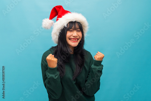 Excited woman in Santa hat clenches fists celebrating happiness Ideal for holiday sales promotions and cheerful visuals