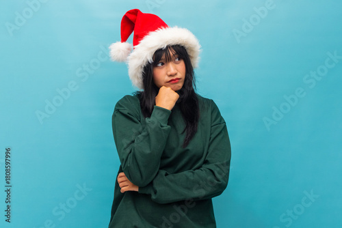 Thoughtful woman in Santa hat rests her chin looking pensive Ideal for creative Christmas campaigns and marketing visuals