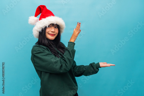 Smiling woman in Santa hat presents product space with one hand Ideal for Christmas sales and festive marketing visuals