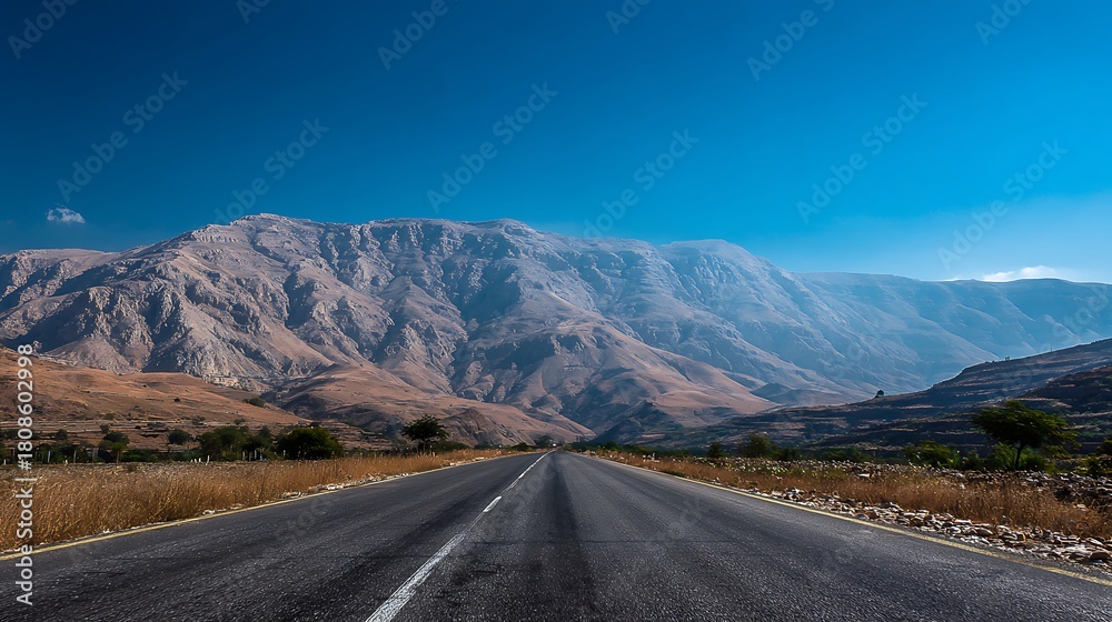 Naklejka premium Awesome photo of road leading to the mountains on a sunny day with clear blue sky.