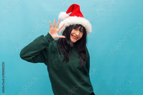 Woman in Santa hat waves hand cheerfully with bright smile Ideal for Christmas greetings and lifestyle promotions