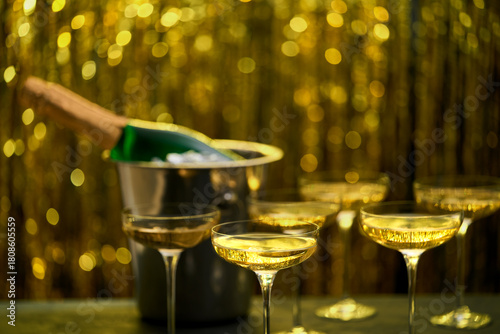 Bottle of champagne in a bucket with ice and glasses on blurred golden stylish background. Space for text.